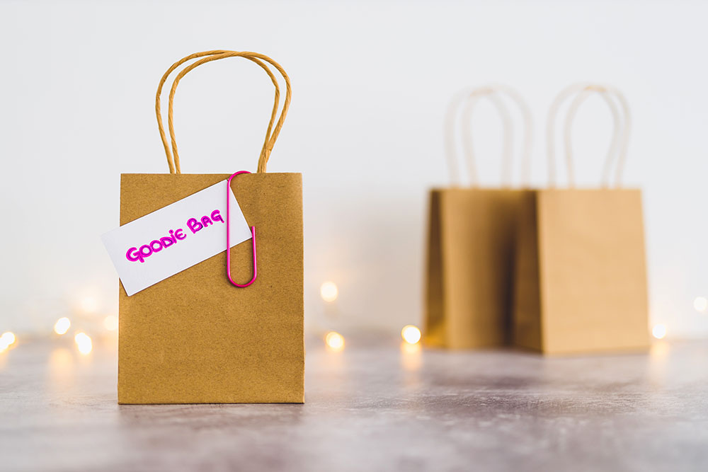 free samples and gifting conceptual still-life, shopping bag with price tag with Goodie Bag text on it and other bags in the background shot at shallow depth of field with bokeh and fairy lights