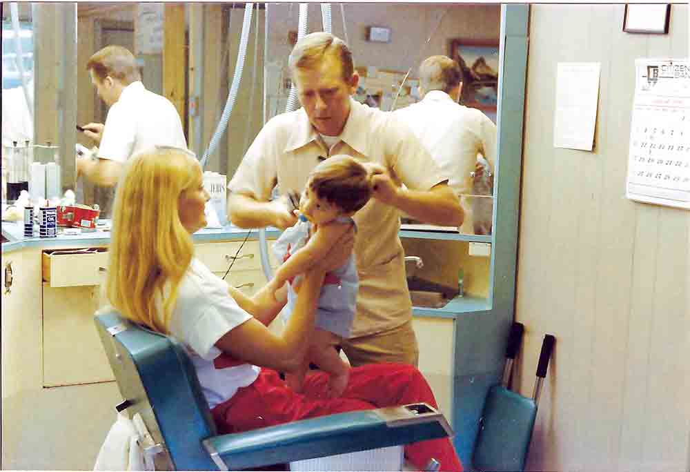 Claude Gulley, in August 1986, cuts a young Jeremy Nichols’s hair. Jeremy’s mother, Becky, holds him still.