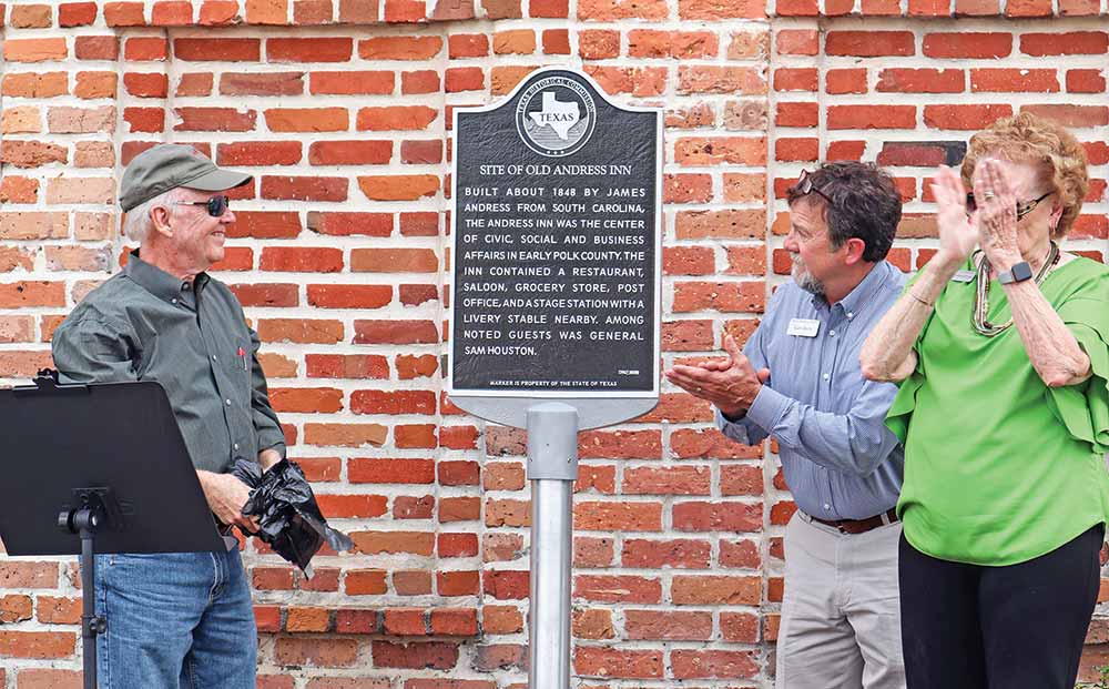Howard Davis unveils the new replacement Texas Historical Marker at the site of the old Andress Inn, Polk County’s first hotel, while Gary Davis and Joyce Johnston watch and applaud. Howard is a descendant of James Andress, owner of the hotel. Gary is a cousin of Howrd’s and a member of the Polk County Historical Commission. Also a member of the Polk County Historical Commission, Joyce serves as the marker chairperson. Photo by Emily Banks Wooten