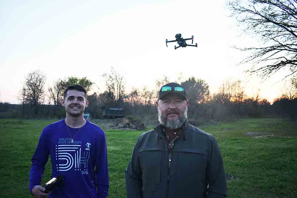 Logan Rice (lt) and his dad Lawrance Rice with their drone hovering in the background, about to scout a distant field for wild hogs.   Photo by Luke Clayton